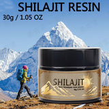 A jar of SHILAJIT resin in front of a mountainous backdrop with a hiker in the distance. The label on the jar indicates the product is a 'Purifying Himalayan resin gift' and provides additional details about the product.