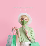 Woman in green outfit with face mask holding a 360-degree beauty instrument against a pink background